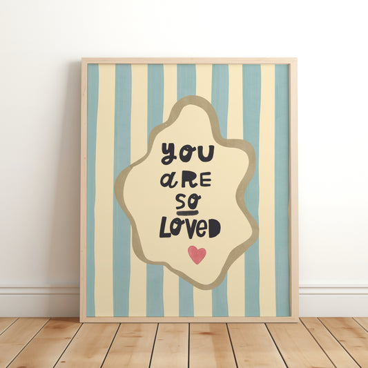 Nursery wall art print with the phrase “You Are So Loved” in playful black lettering, inside an organic cream frame with a gold outline, set over blue and cream vertical stripes and a small red heart.